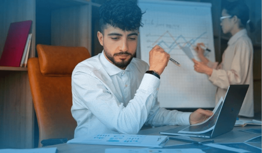 Accountant reviewing financial documents at a desk with charts on a whiteboard